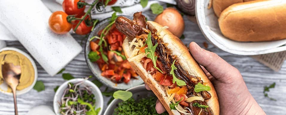 Hot dog s karamelizovanou cibulí, křupavou slaninou, čedarem, rajčetem a hořčicí